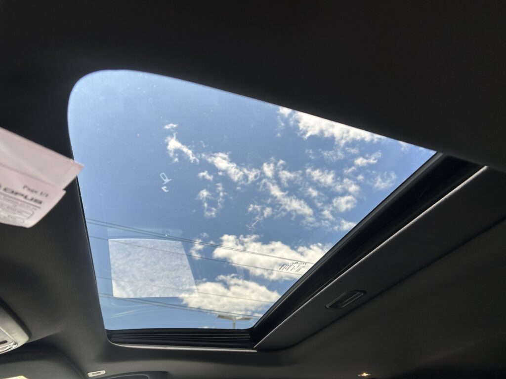 Open panoramic sunroof view showing blue sky and white clouds from inside a car.