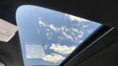 Open panoramic sunroof view showing blue sky and white clouds from inside a car.