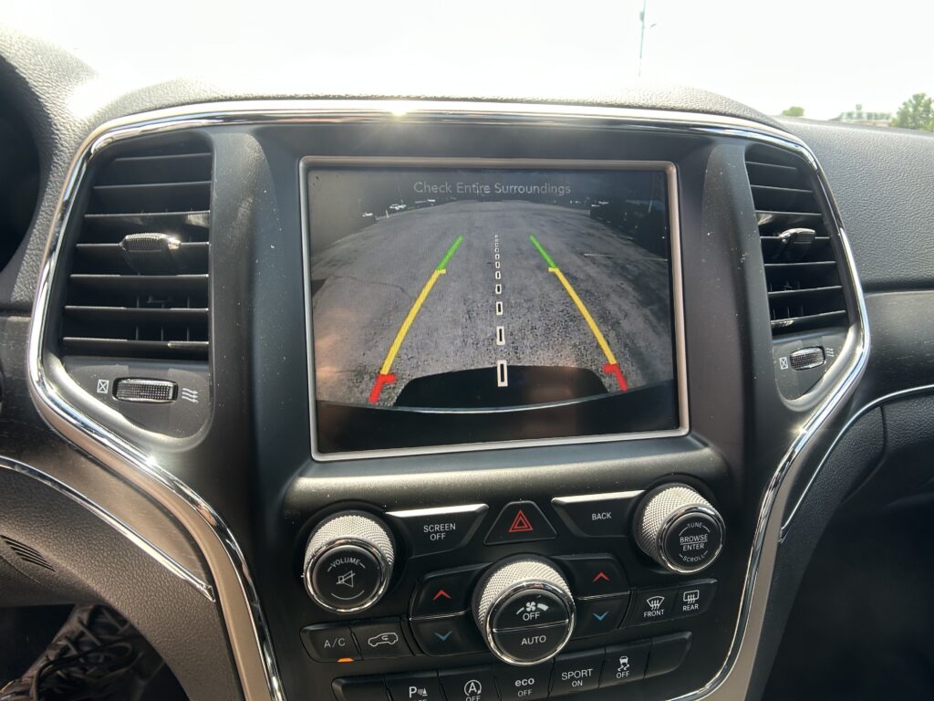 Car dashboard screen showing rearview camera with colored guidance lines for parking.