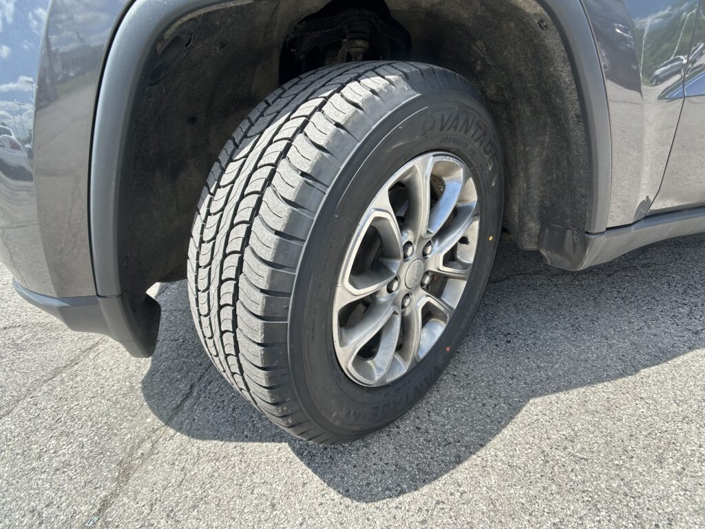 Close-up of a car tire and alloy wheel in the wheel well, showing tread and dirty surroundings.