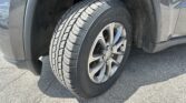 Close-up of a car tire and alloy wheel in the wheel well, showing tread and dirty surroundings.
