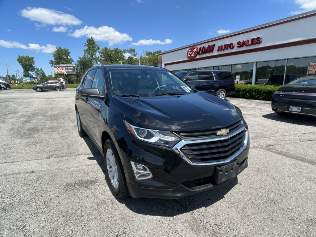 Front-left view of a black Chevrolet SUV parked in a car lot in front of EZ Loan Auto Sales on a sunny day with a white building and blue sky behind. (Informative)