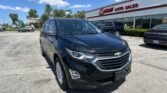 Front-left view of a black Chevrolet SUV parked in a car lot in front of EZ Loan Auto Sales on a sunny day with a white building and blue sky behind. (Informative)