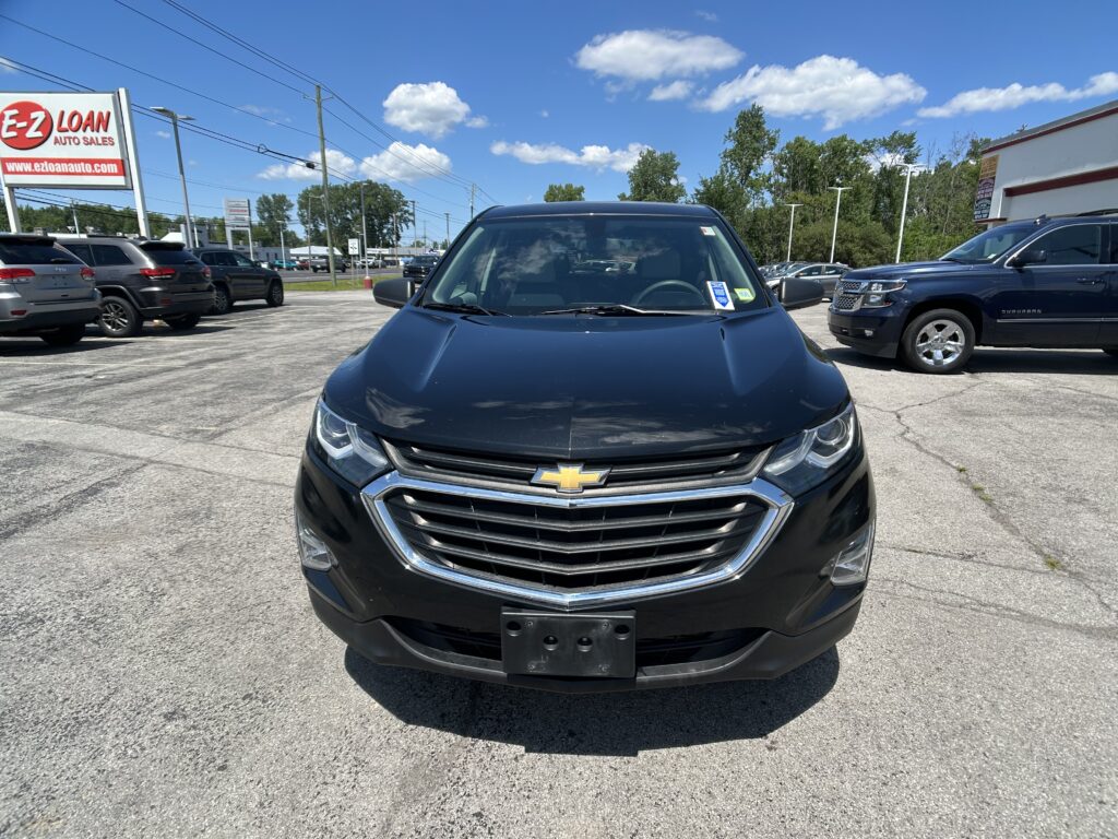 Front view of a black Chevrolet SUV parked in a car dealership lot under a blue sky with other cars nearby.