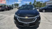 Front view of a black Chevrolet SUV parked in a car dealership lot under a blue sky with other cars nearby.