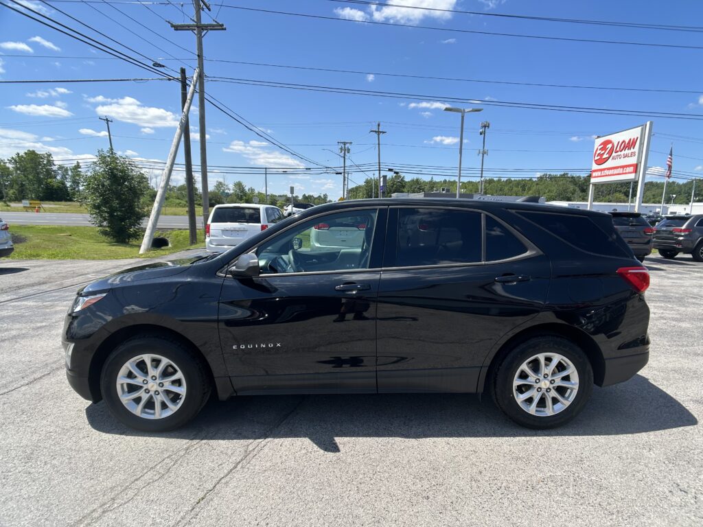 Black Chevrolet Equinox SUV parked in a dealership lot with power lines, blue sky, and an EZ Loan Auto Sales sign in the background.