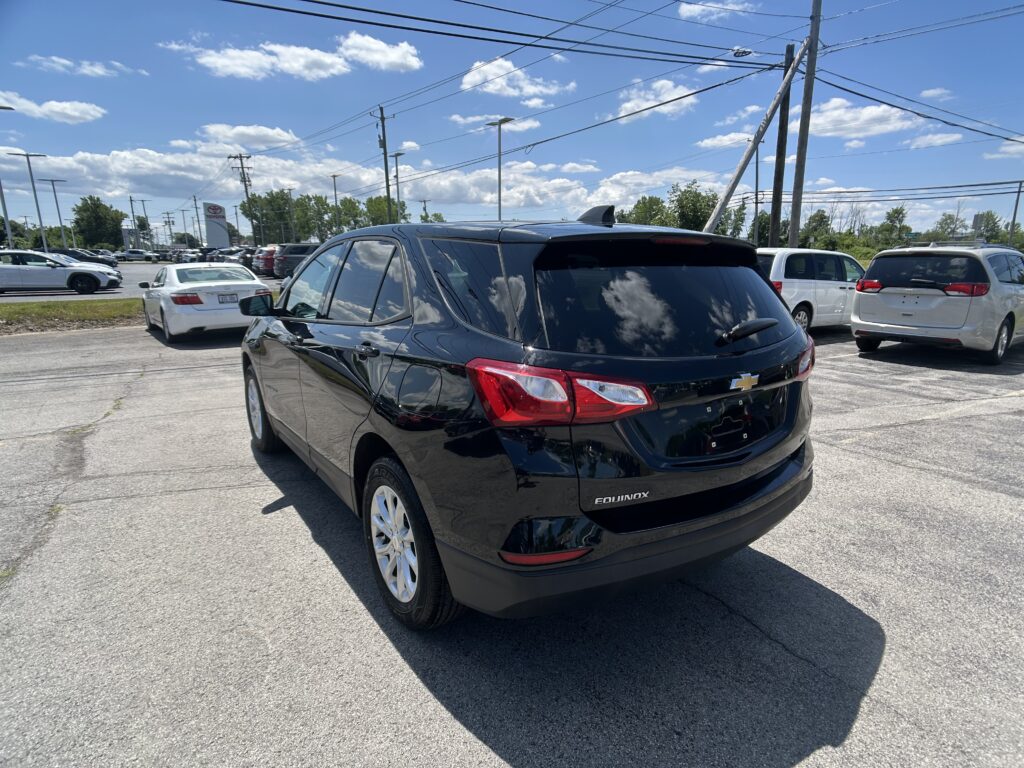 Black Chevrolet Equinox in the foreground of a busy parking lot on a sunny day, with white cars and power lines overhead.