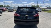 Rear view of a black Chevrolet Equinox in a car dealership lot with other vehicles and a blue, sunny sky above.