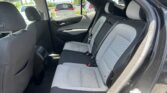 Back row of a car with grey patterned seats and visible seat belts, door open to a sunny parking lot outside the vehicle