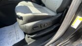 Front passenger-seat area of a car showing seat with light gray fabric, side controls, and open door frame visible at the edge.