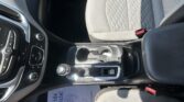 Interior of a car featuring the center console, gear shifter, cup holders, and patterned gray seat upholstery
