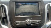 In-dash screen showing a rear camera view with orange parking lines guiding a reverse parking maneuver in a parking lot.