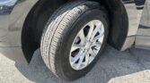 Close-up of a car's front-left wheel, tire, and wheel well on an asphalt surface with reflections in the bodywork.
