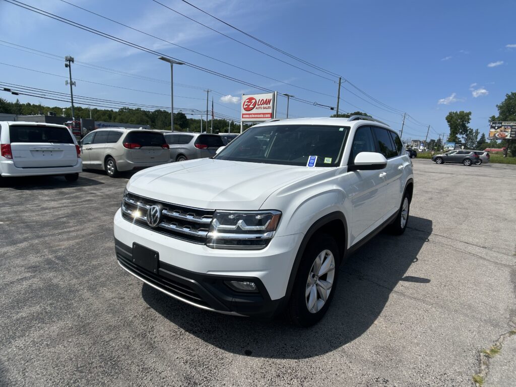 White SUV in the foreground at a sunny car dealership lot with an EZ LOAN Auto Sales sign in the background.