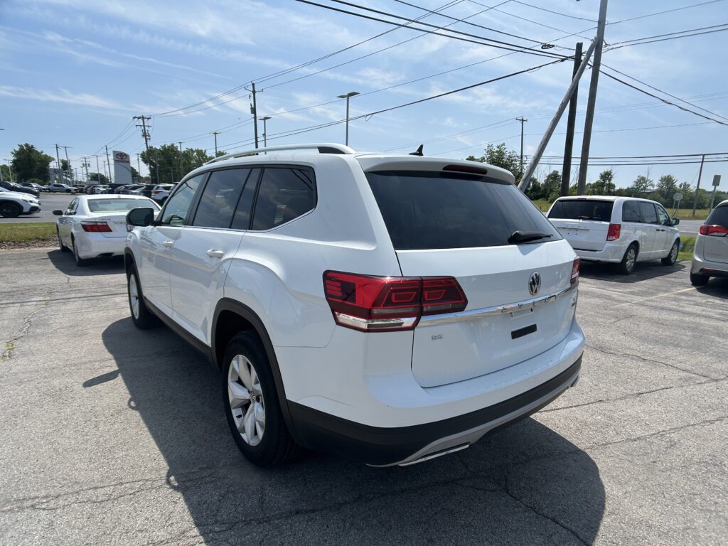 Rear three-quarter view of a white SUV in a dealership lot with other cars, under a blue sky and power lines overhead.