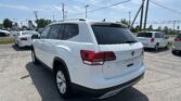 Rear three-quarter view of a white SUV in a dealership lot with other cars, under a blue sky and power lines overhead.