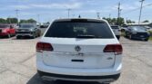 Rear view of a white Volkswagen Atlas SUV in a parking lot with other cars and power lines above.