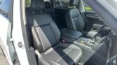 Interior of a white car showing black leather front seats, center console, and the open front passenger door on the left; sunny day outside.