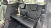 Rear row of black leather seats in an SUV, with seatbelts and a view of a car lot through the window