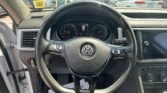 Interior view from the driver's seat in a Volkswagen, with the steering wheel and instrument cluster visible and a parking lot seen through the windshield behind.