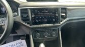 Inside a car cockpit showing a center touchscreen radio display, gear lever in foreground, and part of the steering wheel on the left; paper signs saying 'We Take Pride In Your Vehicle' visible on the passenger side floor.",