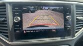 Car infotainment screen displaying the rearview camera view with colored guide lines over a parking lot