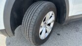 Close-up of a car tire and wheel inside the wheel well of a light-colored SUV, showing part of the fender and suspension.
