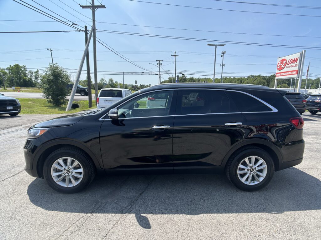 Black Kia SUV in a car dealership lot with power lines and an EZ Loan Auto Sales sign in the background, sunny day