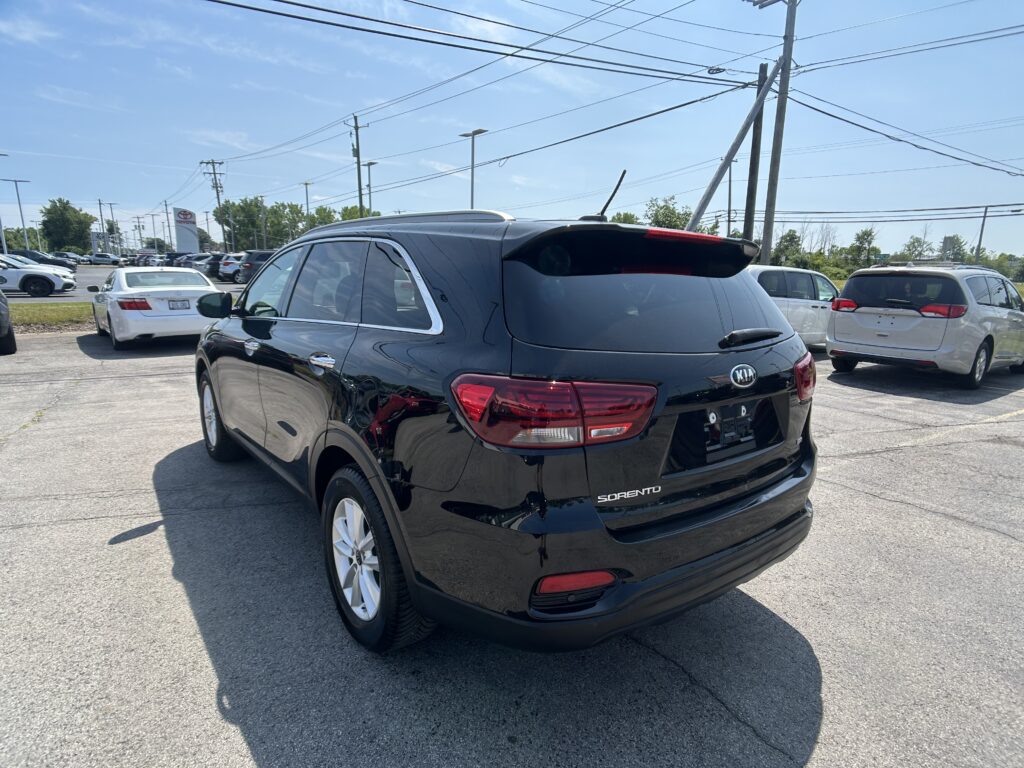 Rear three-quarter view of a black Kia Sorento SUV parked in a car dealership lot with other vehicles and overhead power lines in the background.