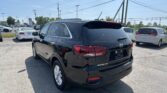 Rear three-quarter view of a black Kia Sorento SUV parked in a car dealership lot with other vehicles and overhead power lines in the background.
