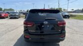 Rear view of a black Kia Sorento SUV in a parking lot with other cars and utility poles in the background, under a blue sky.