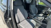 Interior of a car showing the front seats, center console, and steering wheel from the open driver’s side door; black fabric upholstery with stitched patterns.