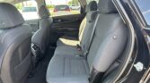 Interior of a sedan's back seat area in gray fabric, showing headrests, seat belts, and door panel; outside parking lot visible through the windows