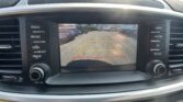 In-car rearview camera display with yellow and red parking lines and a note: 'Check surroundings for your safety' at the top, showing a parking lot.