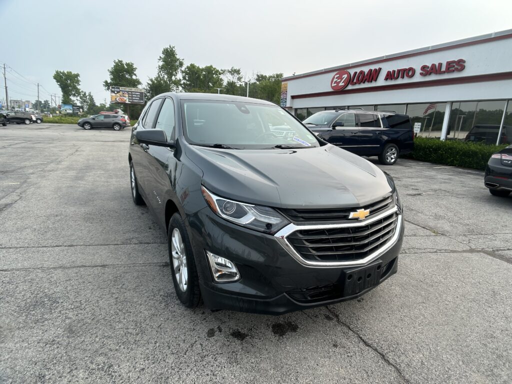 Gray Chevrolet SUV in the foreground at a car dealership lot, EZ Loan Auto Sales in the background.