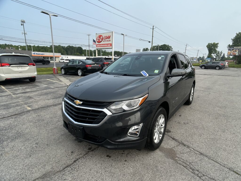 Front-right view of a dark gray Chevrolet SUV parked in a car lot, with an EZ Loan Auto Sales sign in the background and other vehicles around.