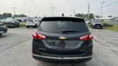 Rear view of a black Chevrolet Equinox parked in a busy dealership lot with other cars around and power lines overhead.