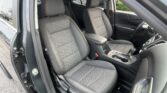 Front car interior with driver and passenger seats, gray fabric upholstery and orange stitching, open door view of the cabin.