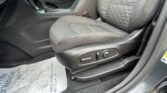 Driver's seat and center console in a dark car interior, showing fabric upholstery, stitching, and gear shifter area with a red seat belt buckle nearby.