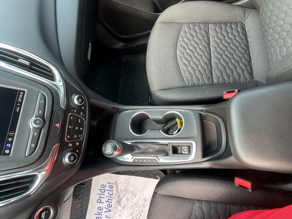 Interior of a car showing center console with gear shift, cup holders, and climate controls beside a patterned front seat close-up