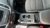 Interior of a car showing center console with gear shift, cup holders, and climate controls beside a patterned front seat close-up
