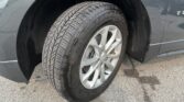 Close-up of a tire and Chevrolet wheel on a dark SUV, with mud on the wheel well and fender edge.