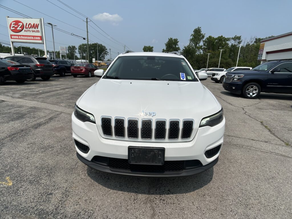 Front view of a white Jeep SUV in a car dealership lot with a tall E-Z LOAN Auto Sales sign in the background on the left.