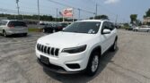 White Jeep SUV in a parking lot with other cars, power lines, and a red EZ LOAN sign in the background under a blue sky.