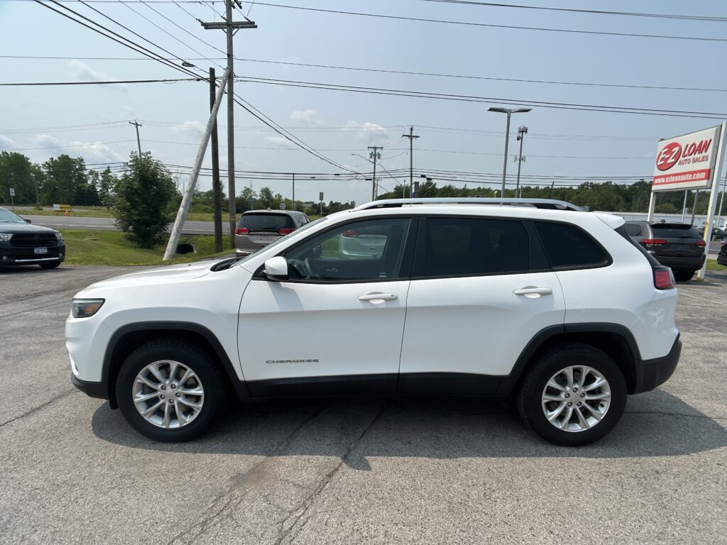 White SUV (Chrysler Cherokee) parked in a car lot with power lines overhead and an EZ Loan Auto Sales sign in the background.