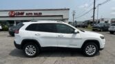 White Jeep Cherokee parked at a car dealership lot, dealership sign reading 'E-Z LOAN AUTO SALES' in the background