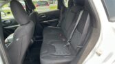 Back seat area of a dark fabric car interior with three seat belts and headrests visible in daylight outside the windows.