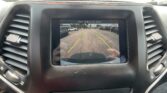 Car infotainment screen displaying rearview camera view with colored parking lines in a parking lot.