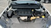 Car engine bay with the hood propped open in a parking lot, showing the engine cover and visible fluid reservoirs.