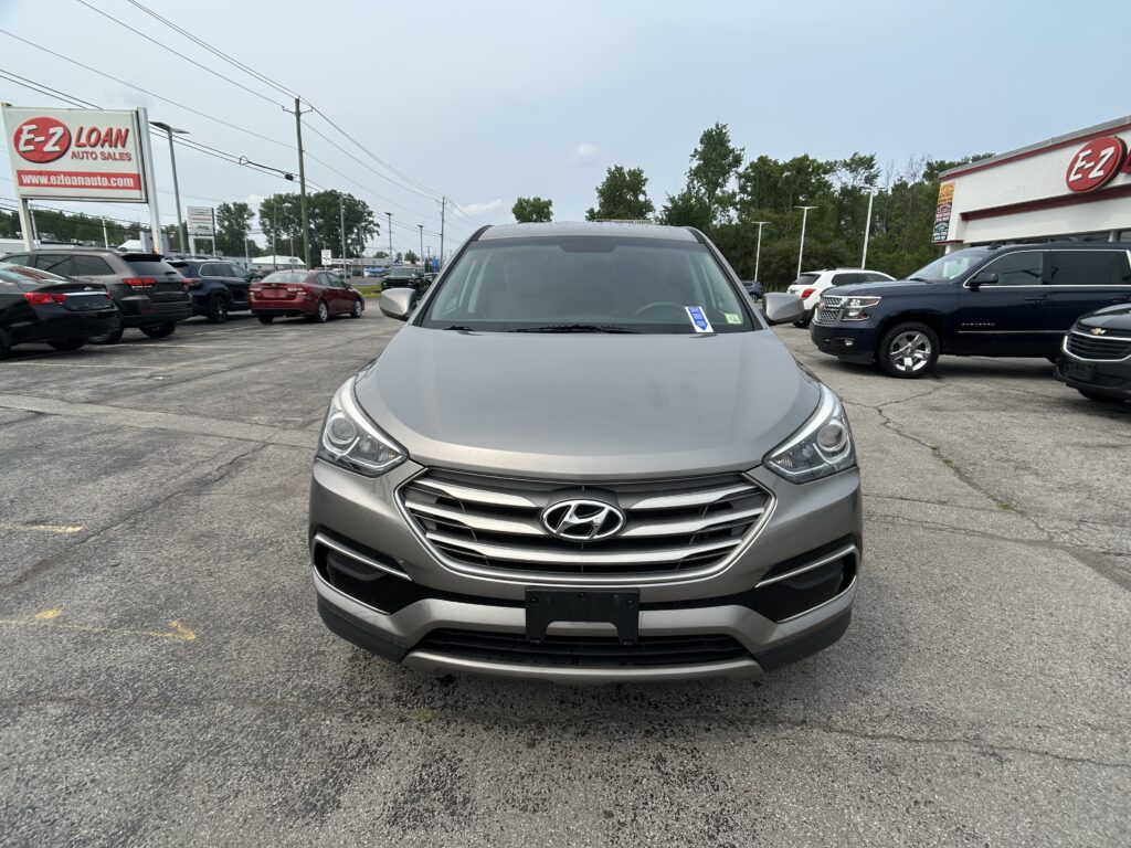 Front view of a gray Hyundai SUV parked in a car dealership lot with other vehicles and an EZ LOAN Auto Sales sign in the background.